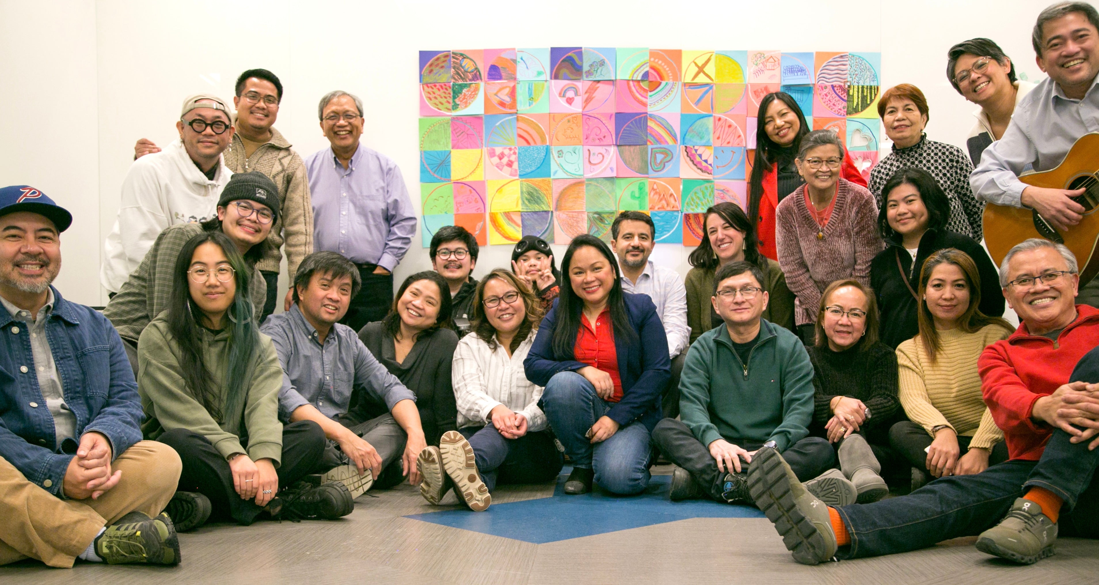 Group of people posing in front of a colorful quilt on a wall.
