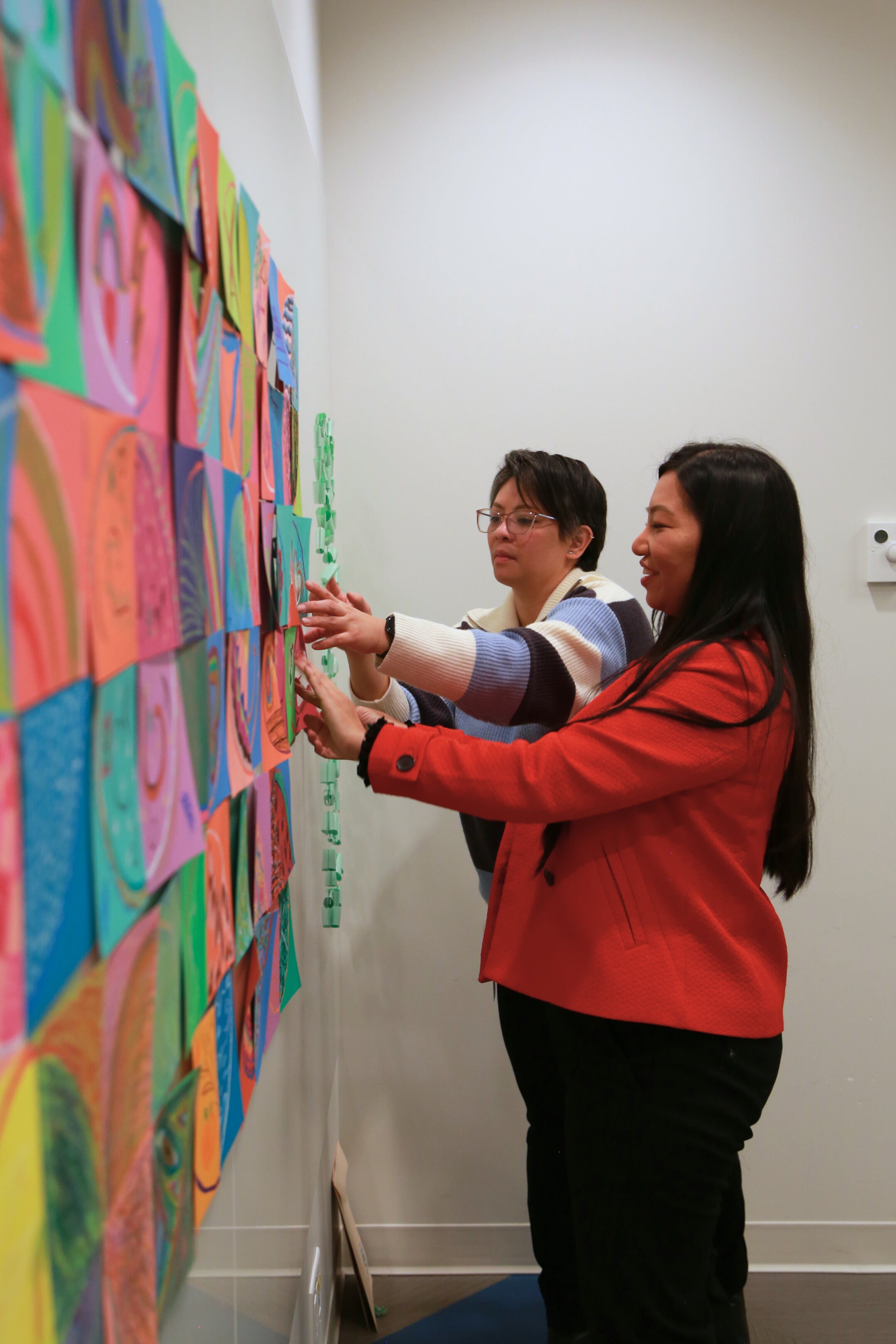 Two people putting together colourful patches on a wall