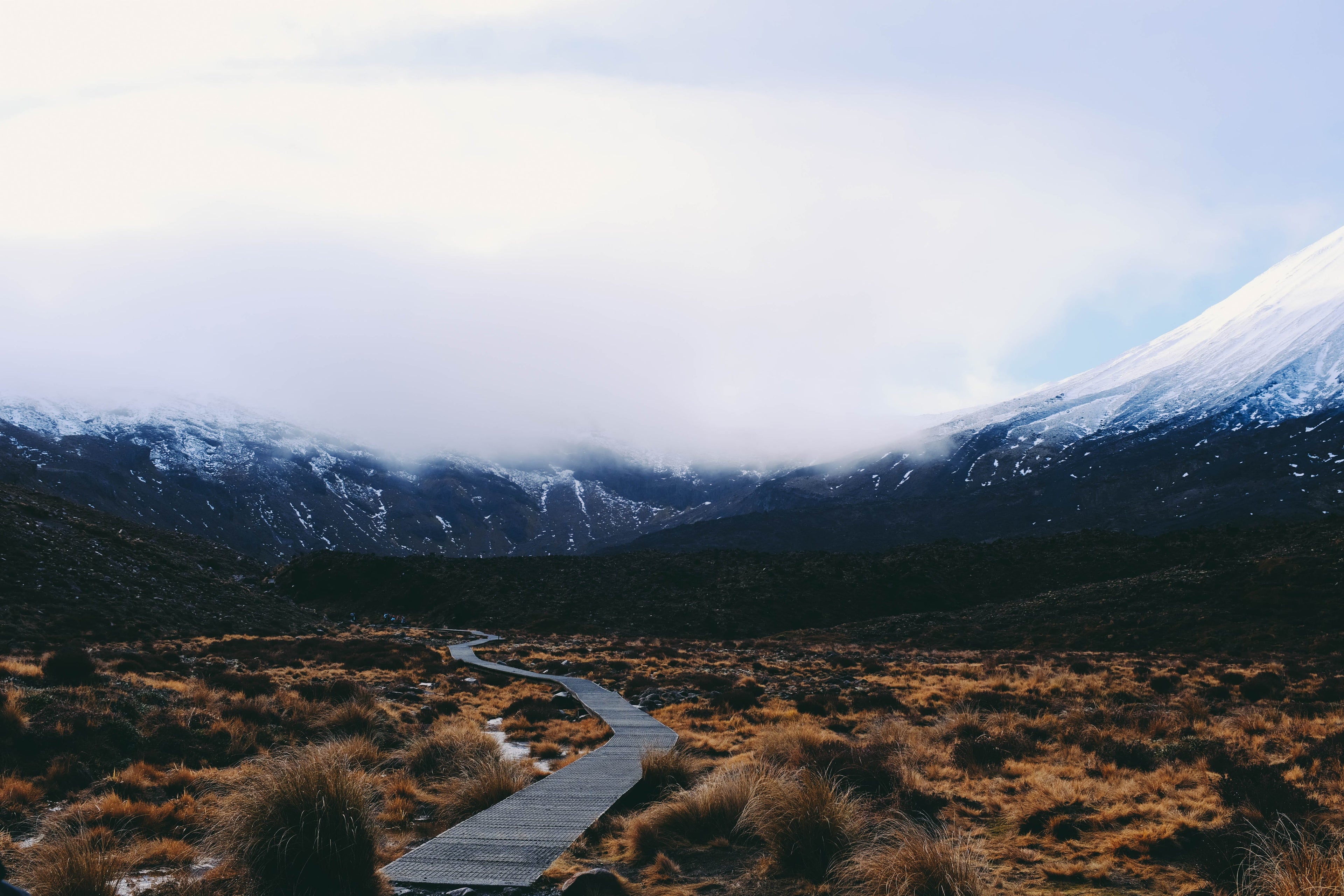 Wooden pathway winding through a mountainous landscape with snow-capped peaks.