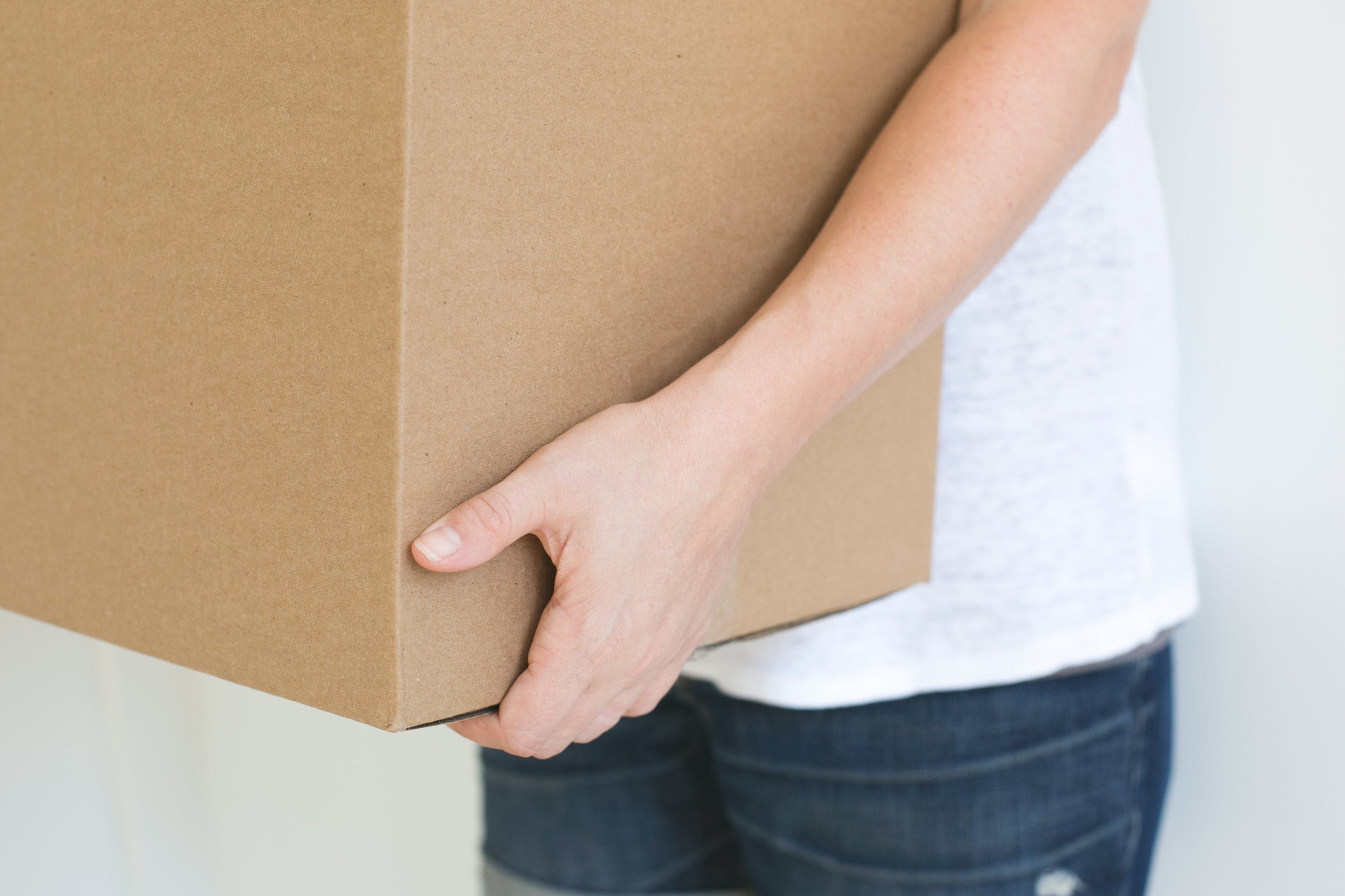 Person wearing white shirt and denim shorts holding box