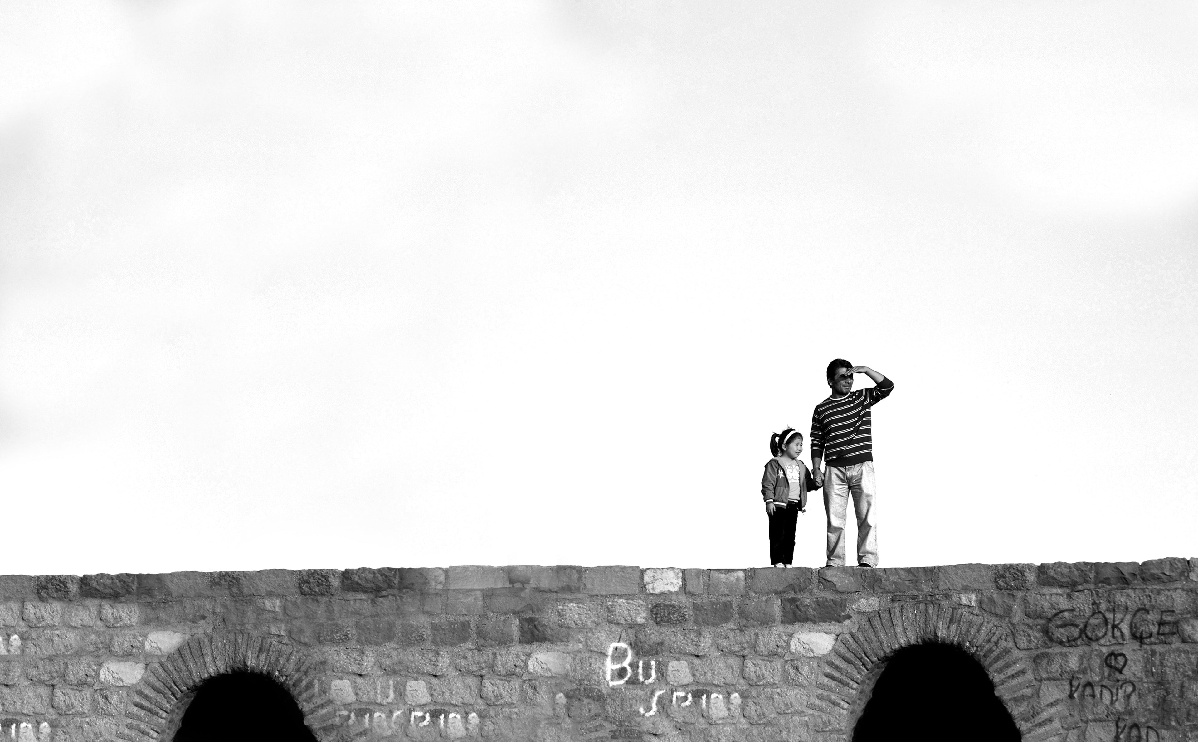 Two people standing on a stone bridge with a minimalistic background
